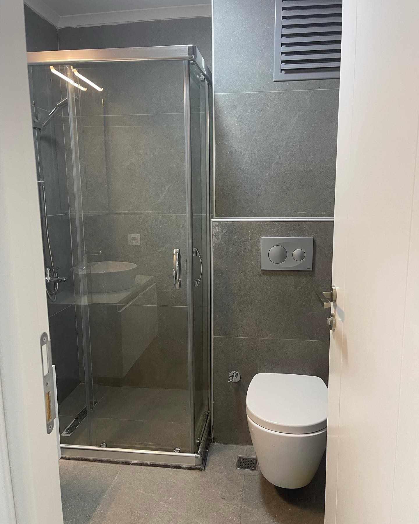 Gri taş kaplama, cam duş bölmesi ve asma klozetli banyo